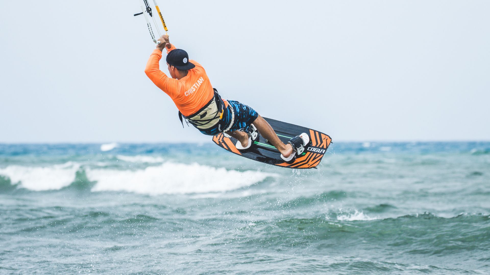 Kitesurfers packed along a wide sandy beach in strong wind.
